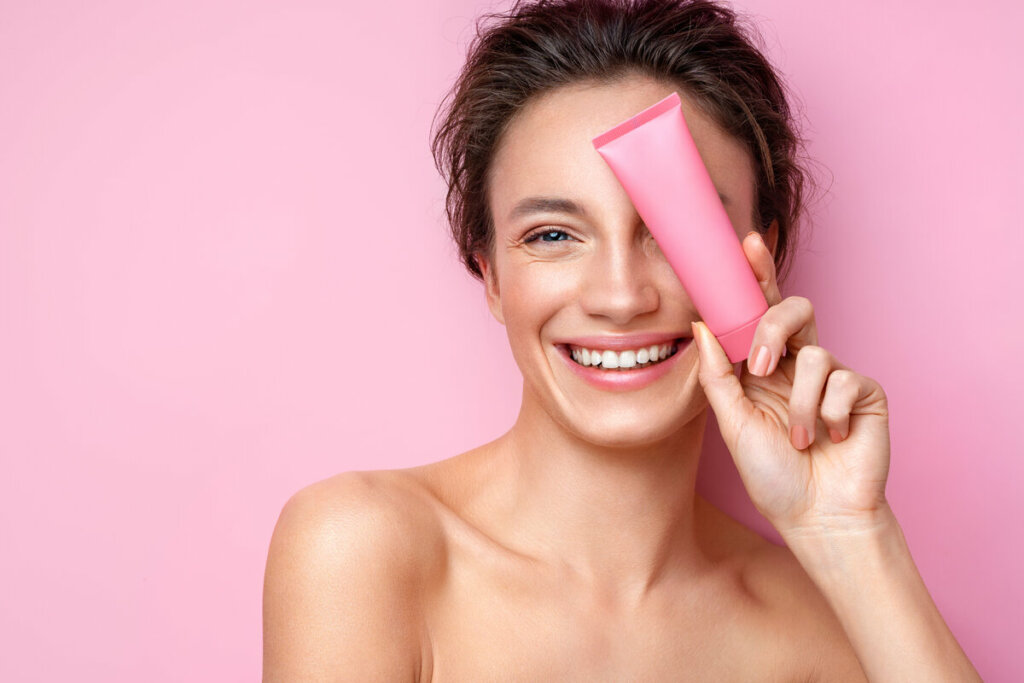 Mulher sorrindo segurando um recipiente rosa em frente ao rosto