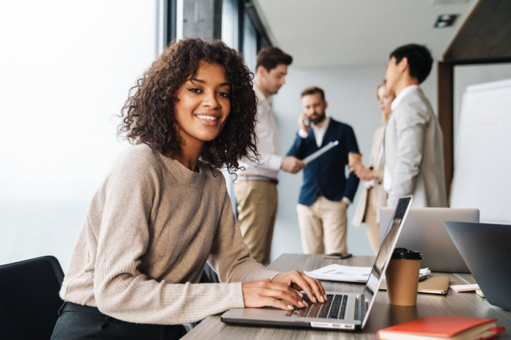 Jovem empresária sentada à mesa do escritório com um grupo de colegas em segundo plano