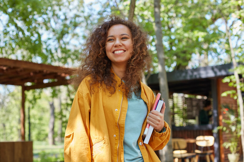 Mulher de blusa amarela sorrindo e segurando livros em um parque