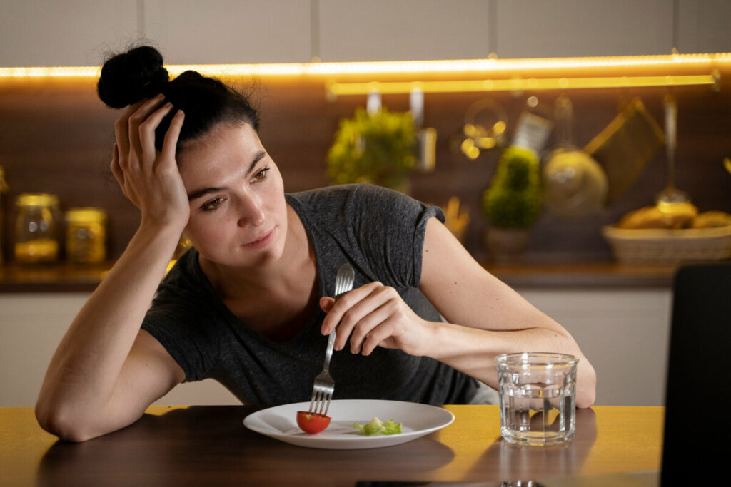 Mulher segurando um garfo em um prato com tomate e alface olhando para o lado 