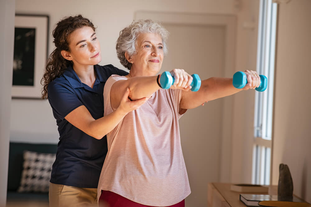 Mulher idosa treinando com fisioterapeuta usando halteres em casa