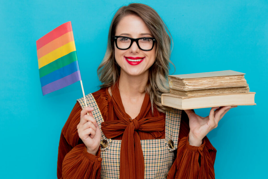 Mulher de óculos segurando livros e bandeira LGBTQIA+