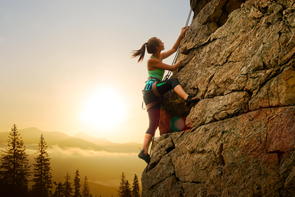 Mulher escalando a rocha alta no pôr do sol nebuloso nas montanhas. Conceito de aventura e esporte radical