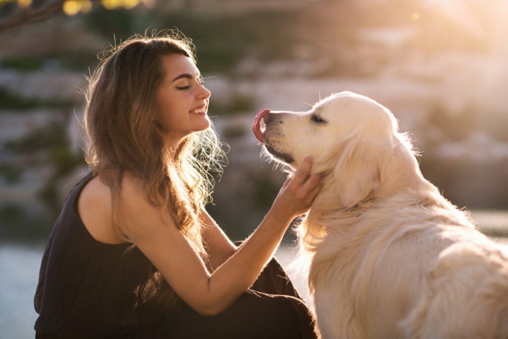 Mulher sorrindo para cachorro grande em ambiente externo.