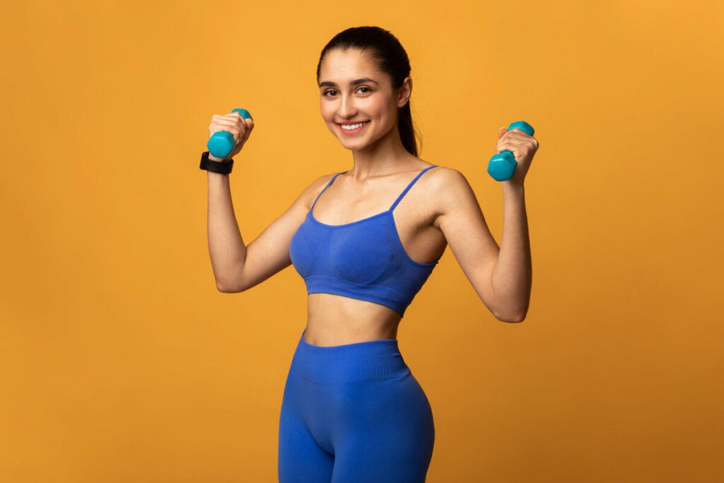 Mulher levantando peso e sorrindo em frente a um fundo amarelo