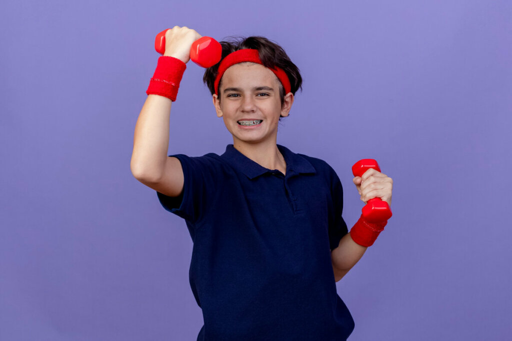 Menino com blusa azul e faixa vermelha na cabeça segurando dois pesoas vermelhos