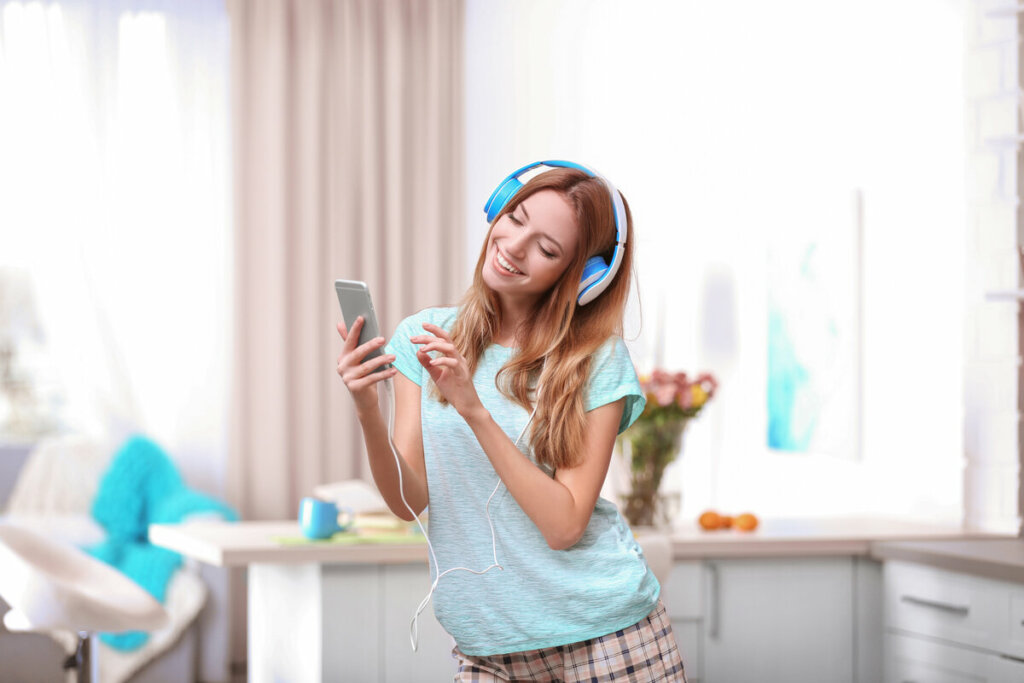Mulher com fone de ouvido azul segurando um celular e dançando
