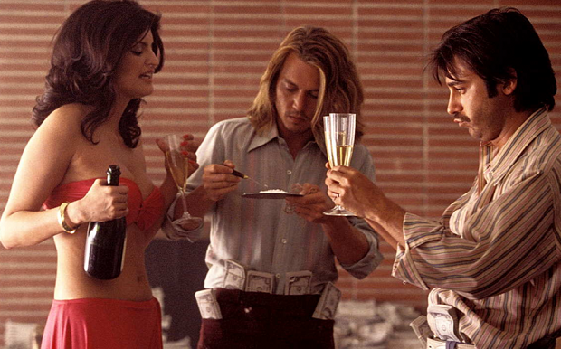 Cena do filme "Blow", personagens em festa com bebida, cocaína e notas de dinheiro. 