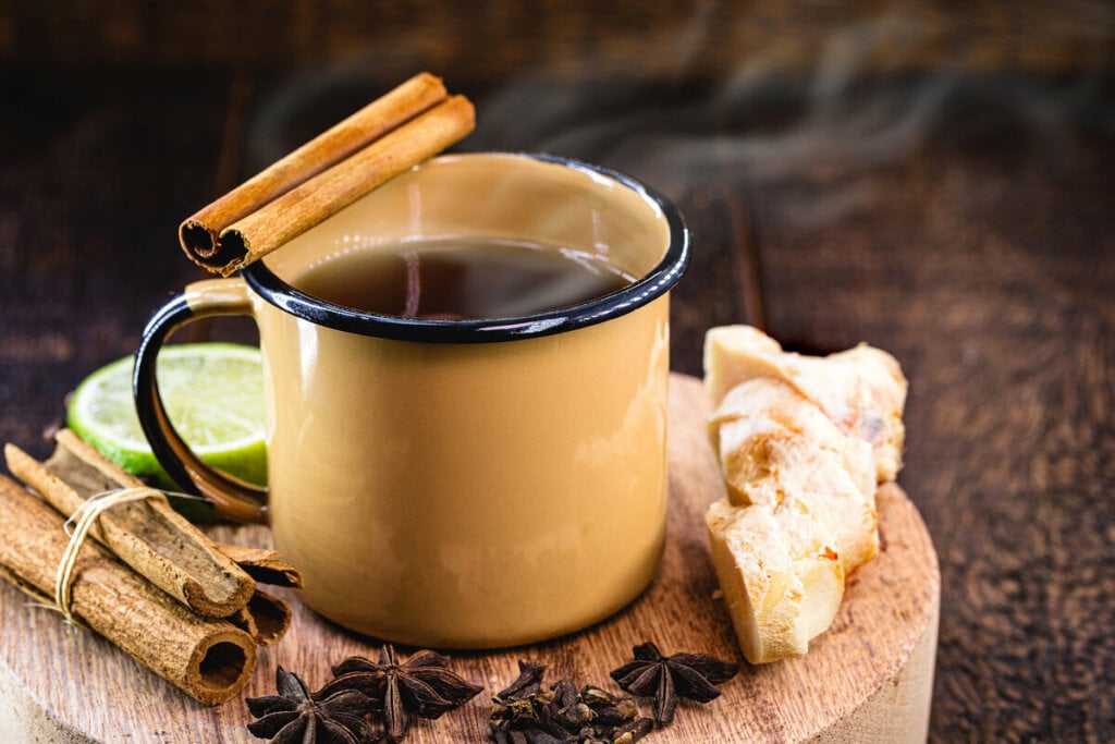 Caneca com quentão em cima de uma mesa de madeira com gengibre, limão, canela e hibisco