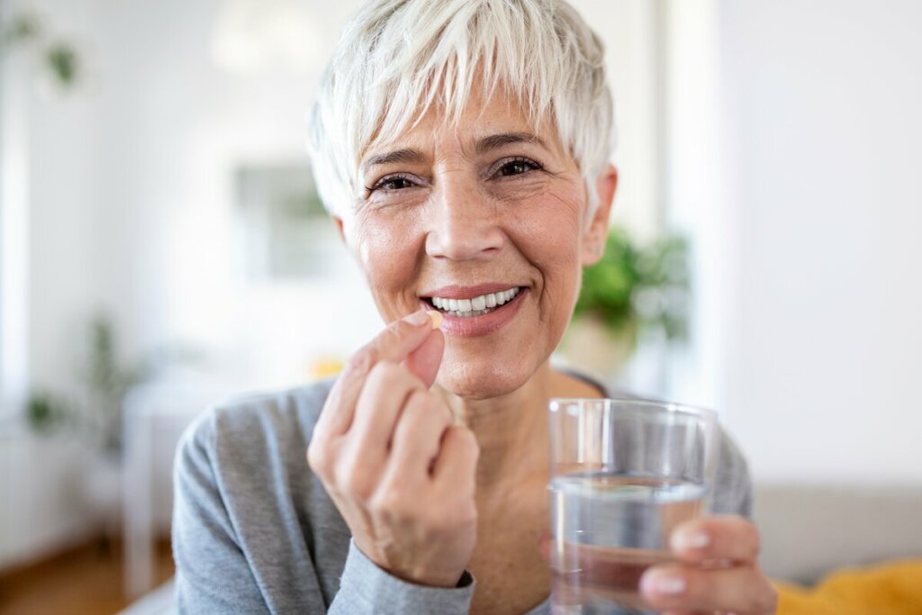 Mulher sorrindo segurando um comprimido e um copo com água