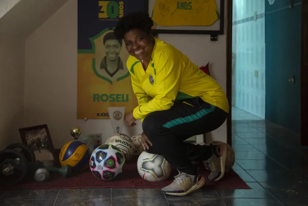 Roseli de Belo sorrindo com a camisa da seleção e bolas de futebol.