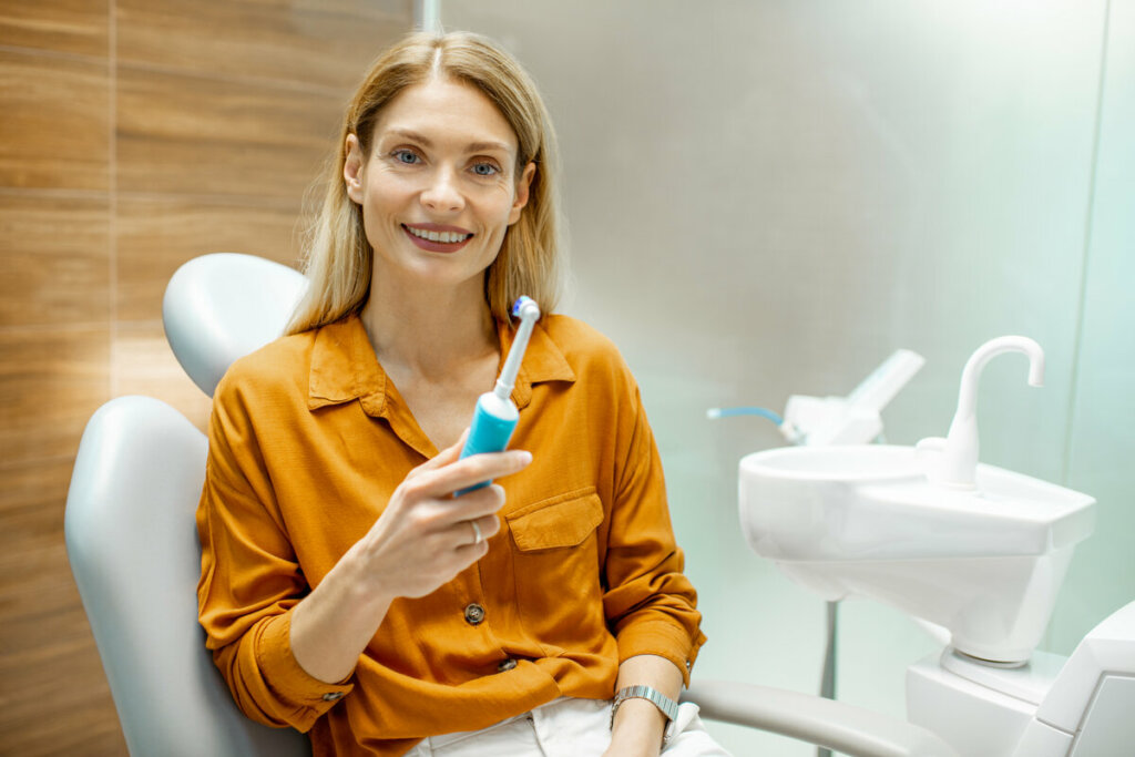 Mulher de blusa laranja sentada, sorrindo e segurando uma escova de dentes