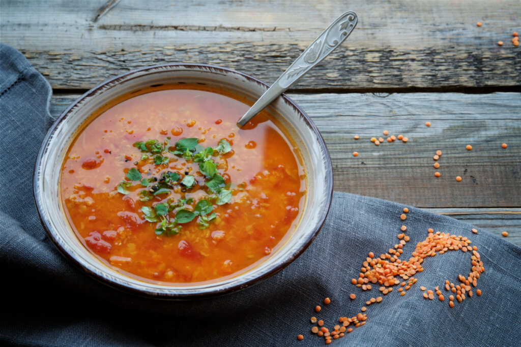 Sopa de lentilha vermelha em recipiente em cima de uma mesa de madeira