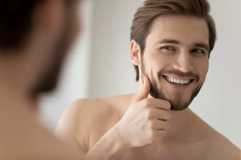 Homem sorrindo olhando a barba no espelho