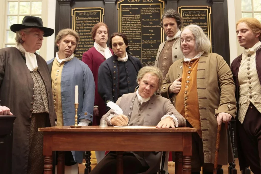 Cena do filme "1776", em que vários homens assinam a Declaração da Independência dos EUA.