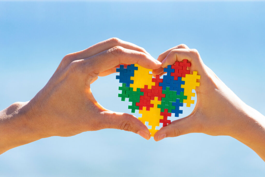 Mãos de criança e adulto segurando um coração colorido, símbolo da conscientização sobre o autismo