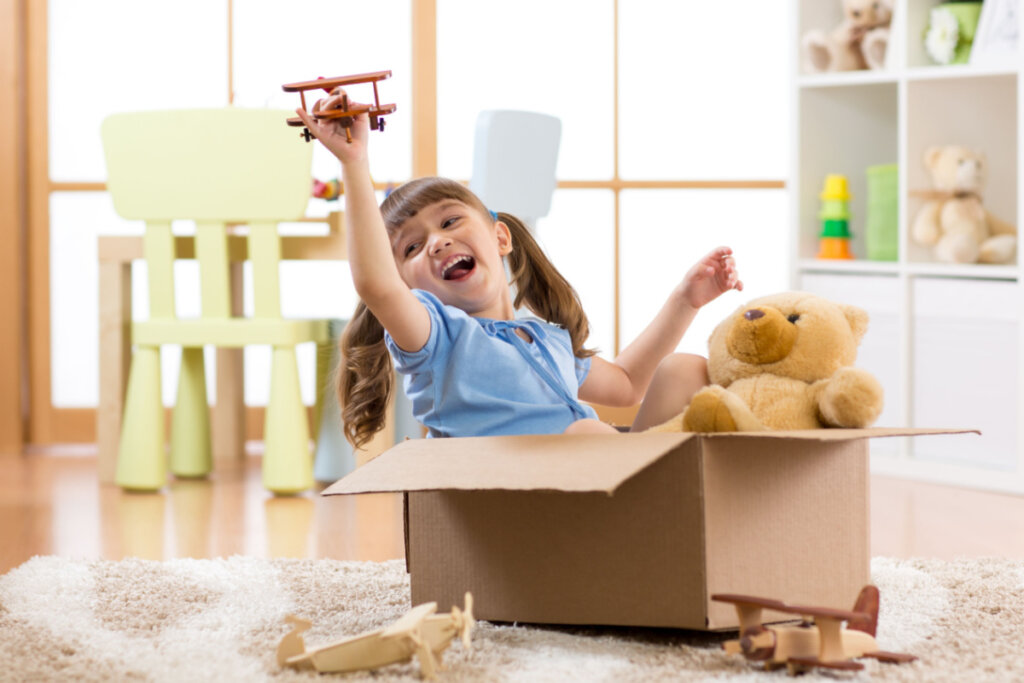 Garota brincando de piloto fingindo estar voando uma caixa de papelão no quarto