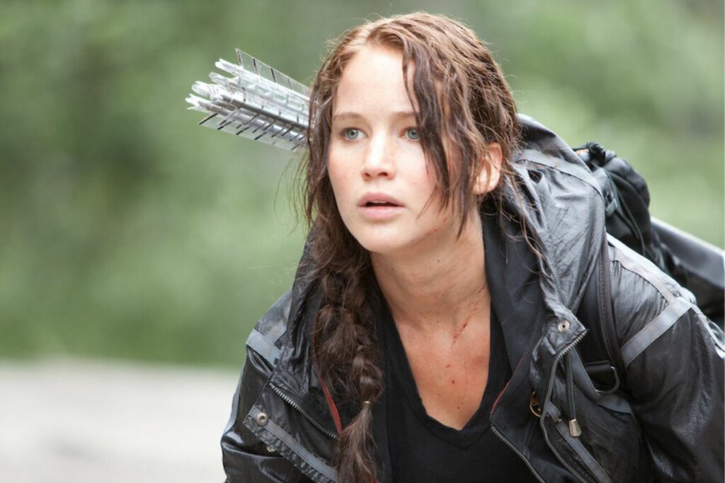 Cena do filme "Jogos Vorazes"; Katniss olhando para frente com flechas em mochila nas costas 