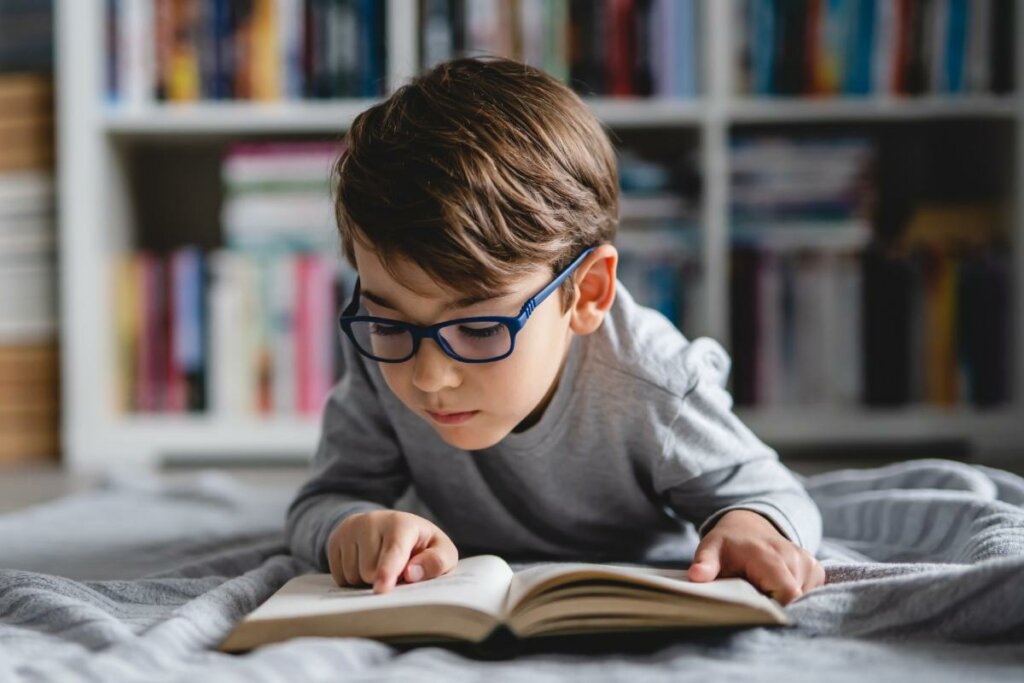 Menino usando óculos deitado lendo livro