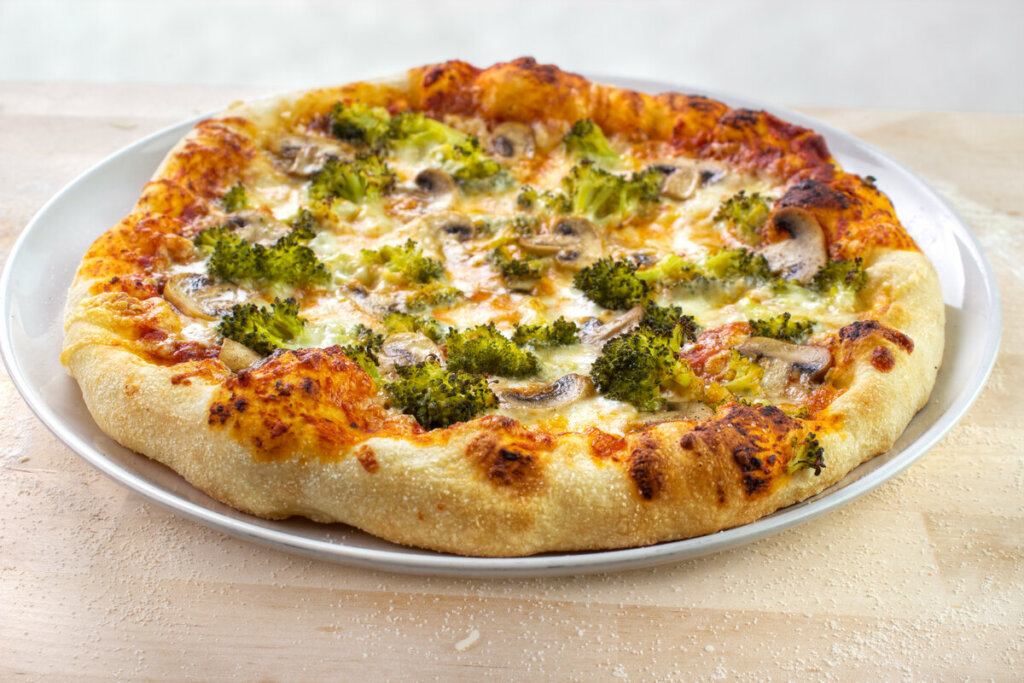 Pizza de brócolis com queijo e cogumelos em cima de uma mesa de madeira