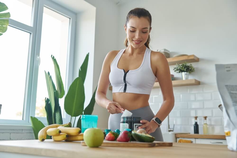 Mulher jovem com roupas esportivas preparando uma vitamina de whey protein com frutas