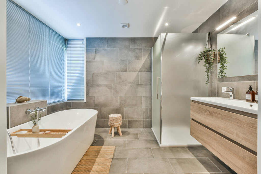 Banheiro com banheira branca, azulejo cinza e móveis de madeira