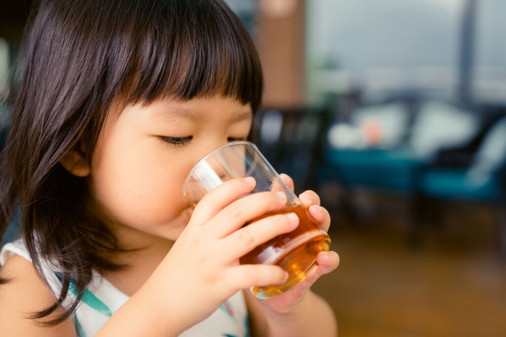 Criança bebendo chá de camomila em copo de vidro. 