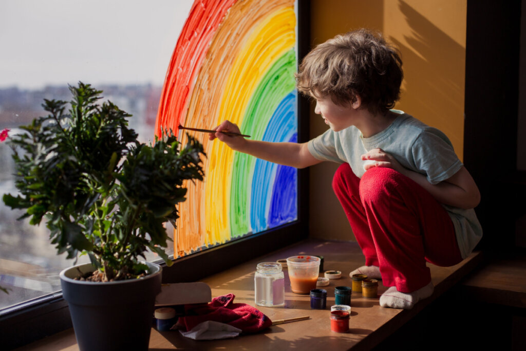 Criança em casa desenha um arco-íris na janela