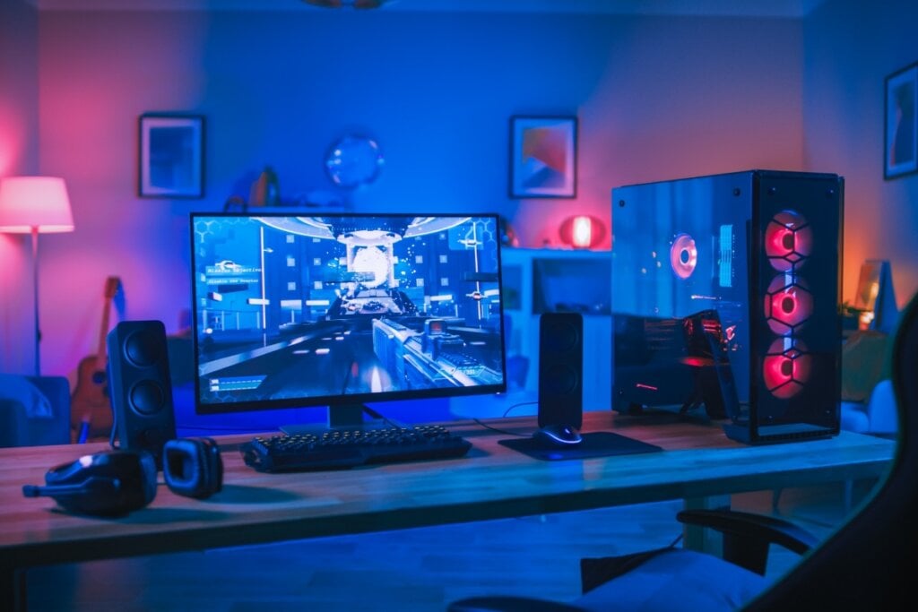 Computador em uma mesa de madeira dentro de um quarto com luz azul e rosa