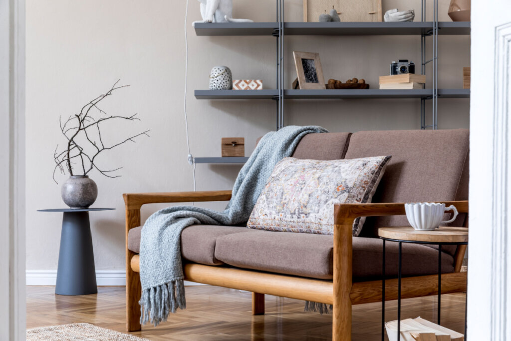 Sala de estar no apartamento aconchegante com sofá de madeira marrom, mesa de centro, estante cinza, travesseiro, xadrez e acessórios elegantes
