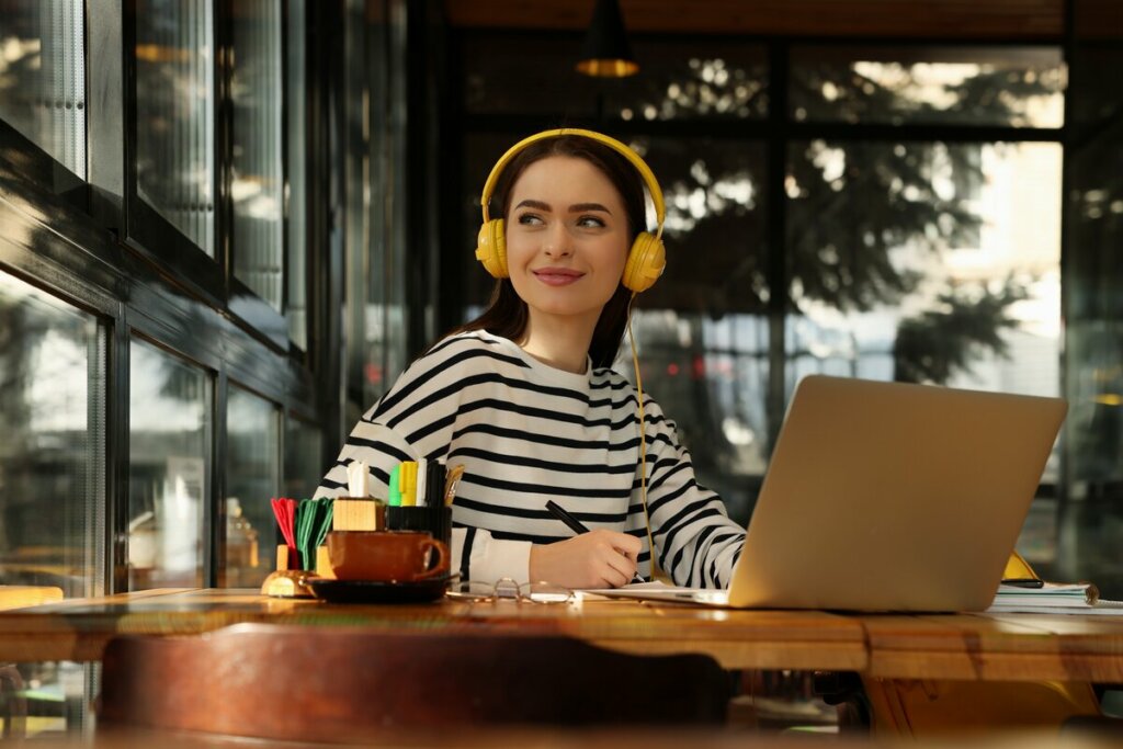 Menina usando fone de ouvido amarelo sentada em frente a um computador estudando