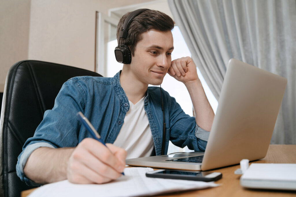 Menino sorrindo usando fone de ouvido estudando em um notebook