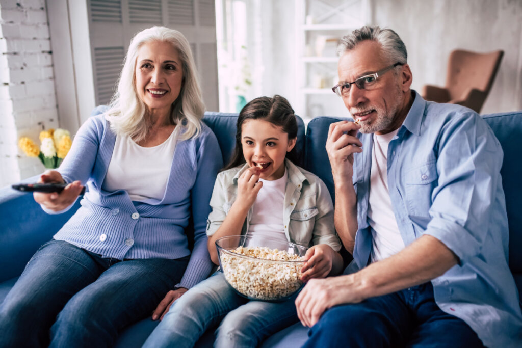 Criança assistindo a filme e comendo pipoca com avós