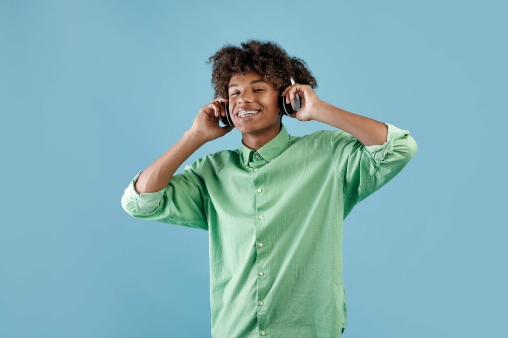 Menino vestindo blusa verde e usando fone de ouvido em frente a um fundo azul