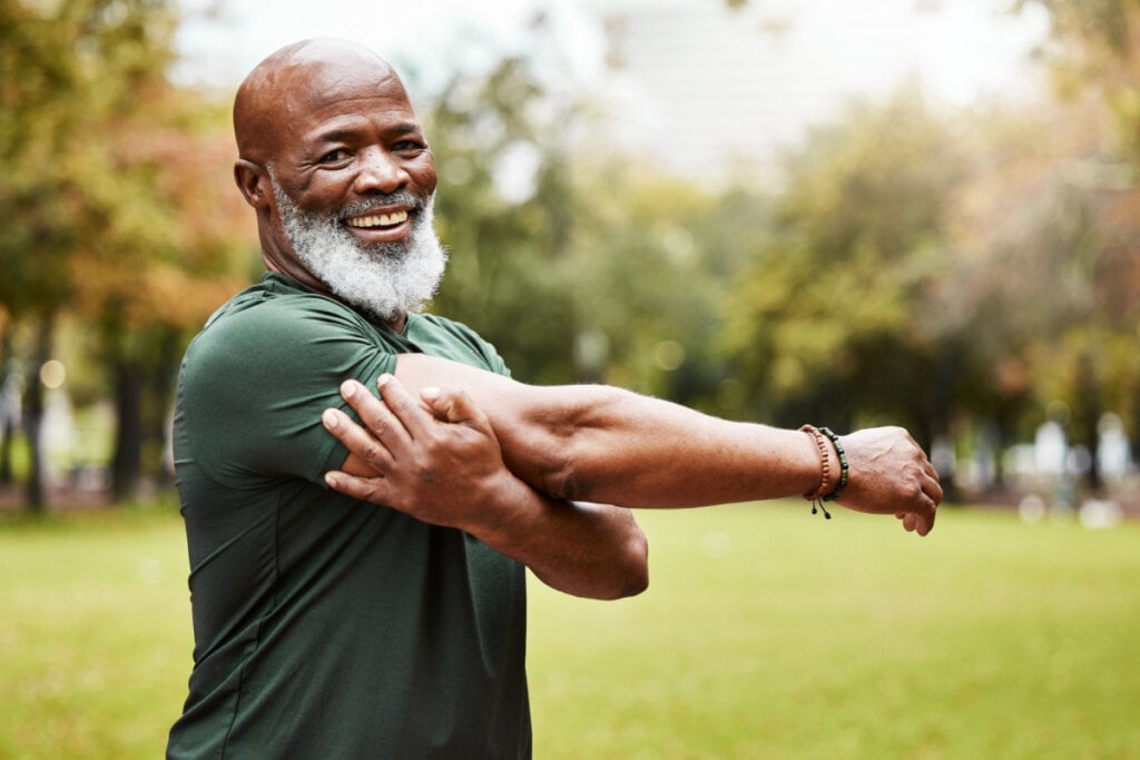 Homem com camiseta verde e barba branca alongando o braço