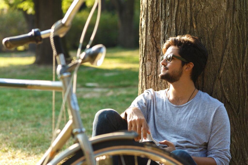 Homem tranquilo encostado em parque ao lado de bicicleta.