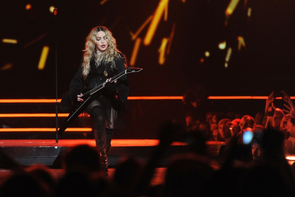 Cantora Madonna tocando guitarra em palco durante show.
