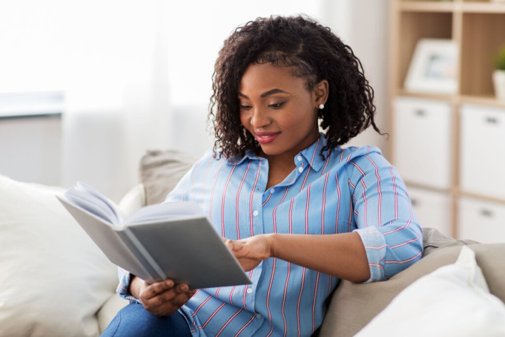 Mulher sorridente lendo livro em casa