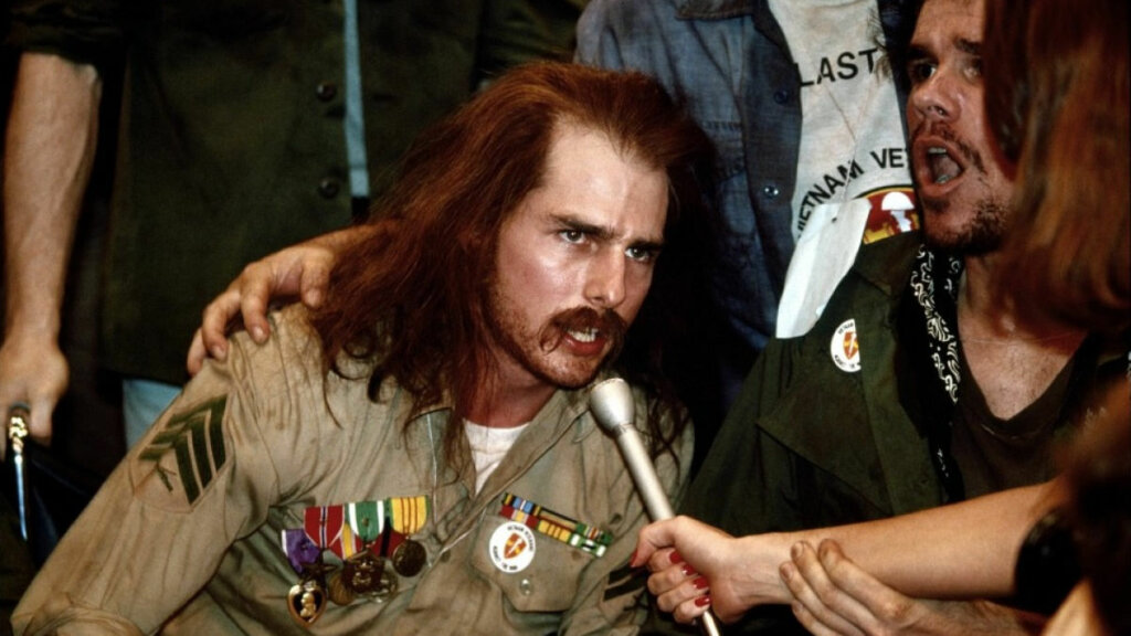 Cena do filme "Nascido em 4 de julho". Tom Cruise com roupa de soldado dos EUA dando entrevista durante protesto.