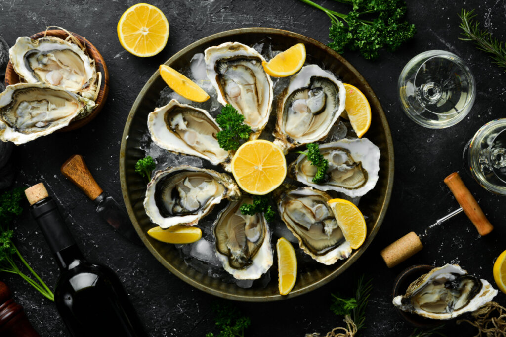 Garrafa de vinho envelhecido e ostras frescas em uma mesa de cozinha escura.