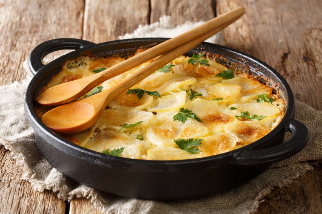 Panela preta com batata gratida com queijo em cima de uma mesa de madeira