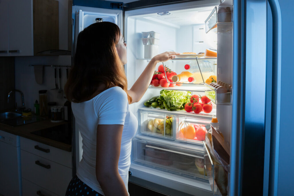 Mulher olhando comidas dentro de uma geladeira