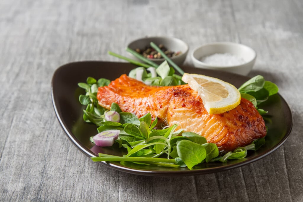 Filé de salmão em um prato preto com salada decorado com uma fatia de limão