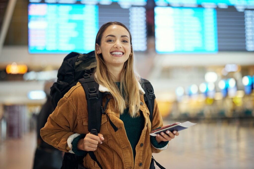 Mulher sorrindo segurando passaporte dentro de um aeroporto