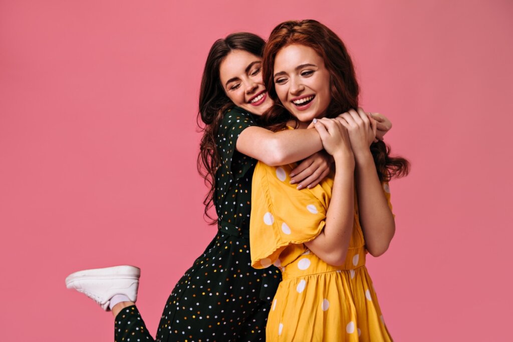Duas mulheres se abraçando em frente a um fundo rosa
