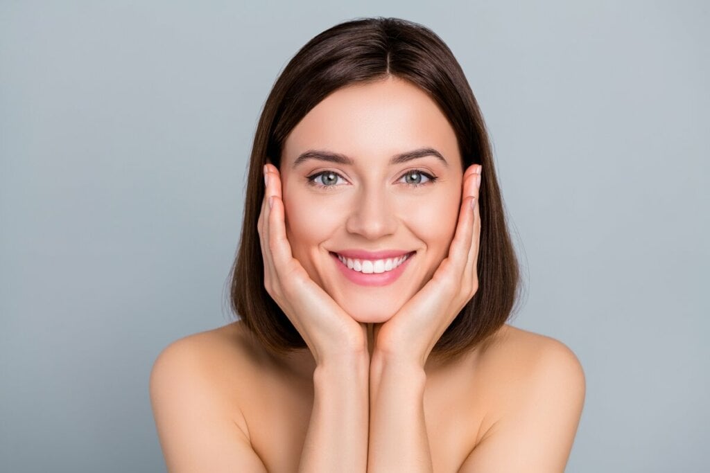 Mulher sorrindo com as duas mãos em baixo do rosto