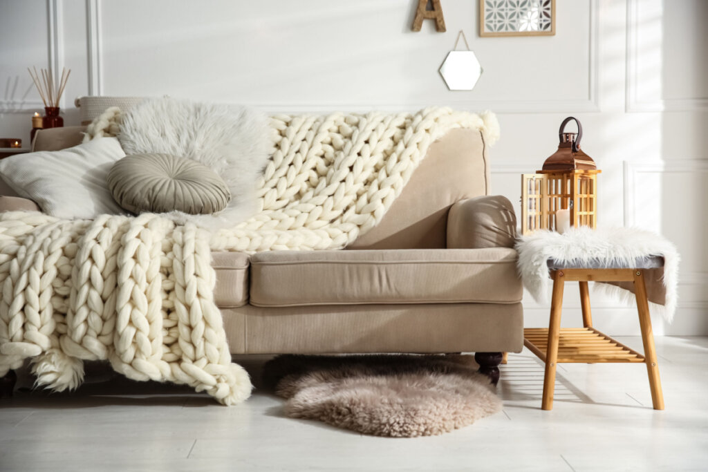 Interior aconchegante da sala de estar com sofá bege, cobertor de malha e almofadas
