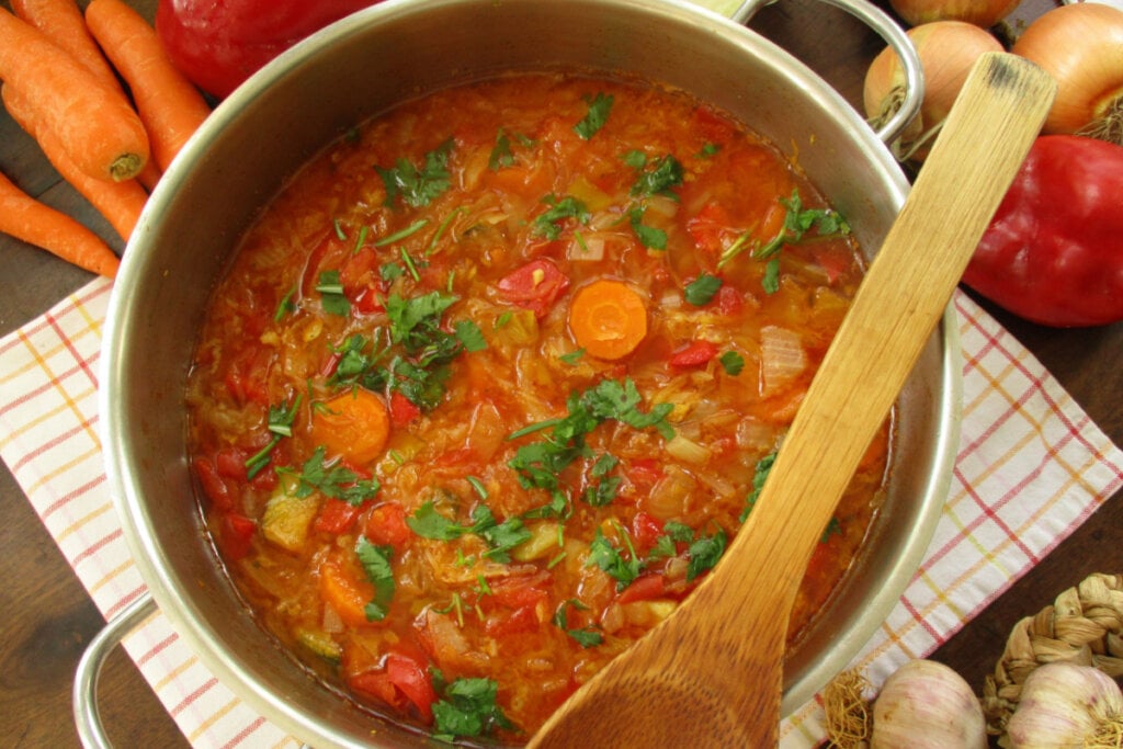 Sopa de repolho colorida em panela ferro com colher de pau e vegetais em volta