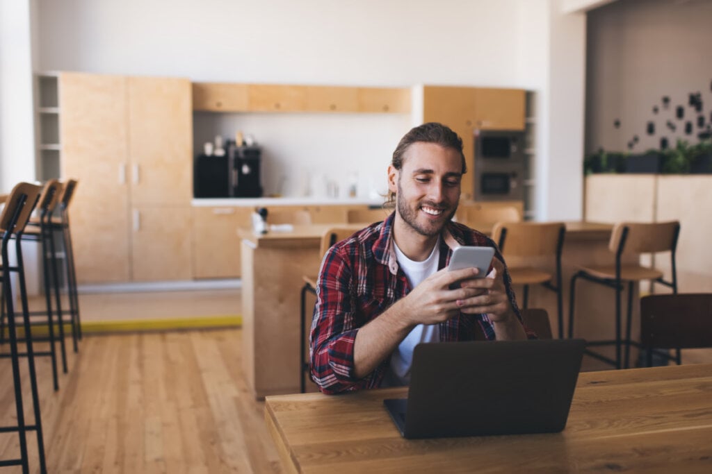 Homem com celular na mão e mexendo no notebook