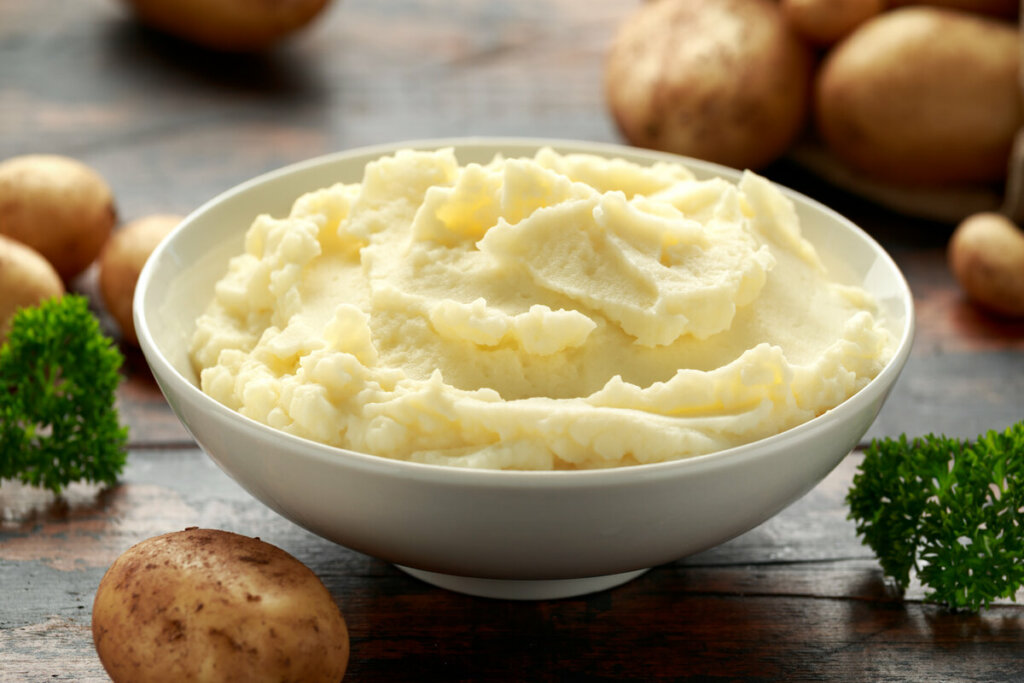 Recipiente branco com purê de batata em cima de uma mesa de madeira